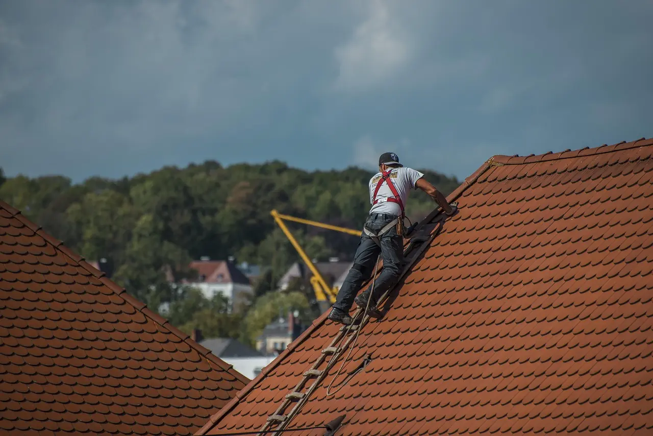 Un couvreur encordé monte sur une toiture en tuiles sous un ciel d'orage