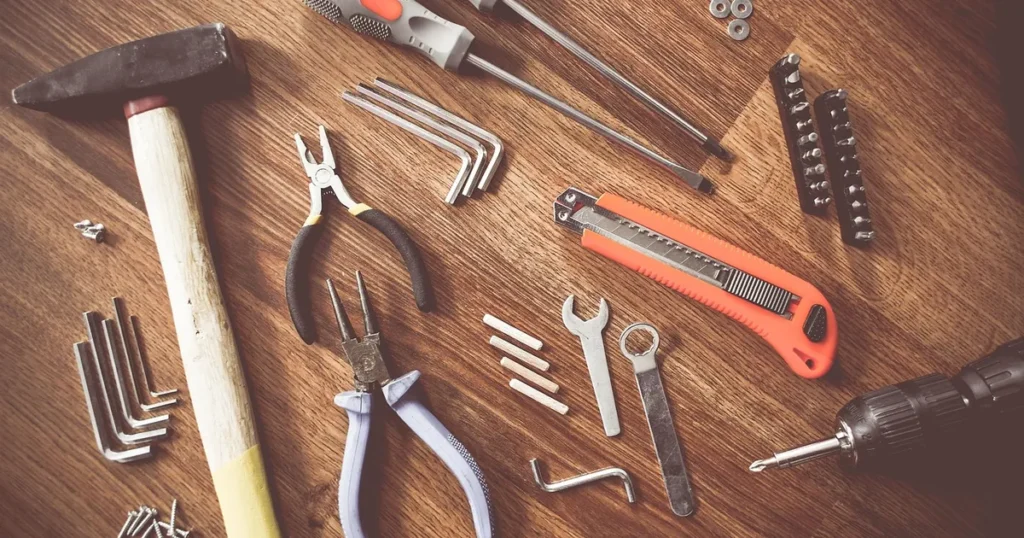 Des outils de plusieurs métiers posés sur un établi en bois : marteau, pinces, cutter, clés et tournevis.