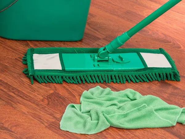 Un balai à plat vert sur un parquet en cours de nettoyage, Nettoyage.