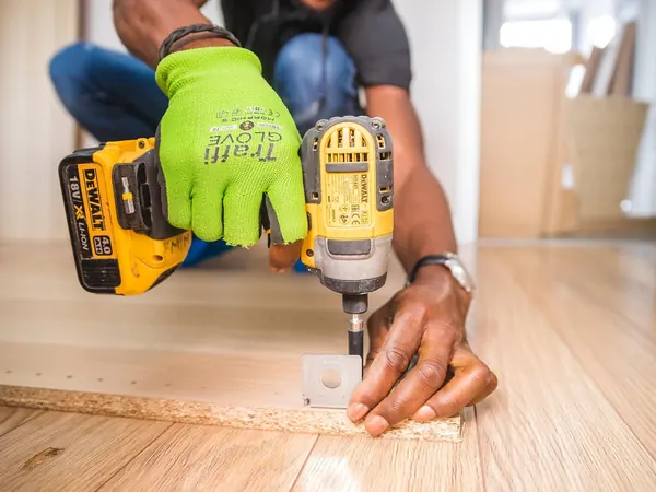Un artisan visse une planche à la perceuse, Petits travaux.