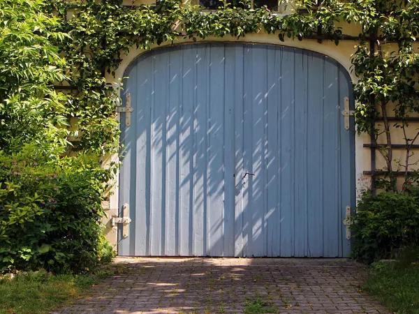 Une porte de garage bleue entourée de verdure, Portes de garage.