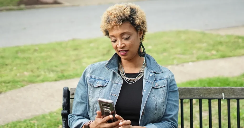 Une femme assise sur un banc consulte son téléphone.