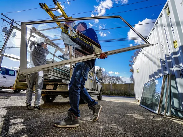 Un ouvrier porte un châssis de fenêtre sur un chantier, Réparation de fenêtres.