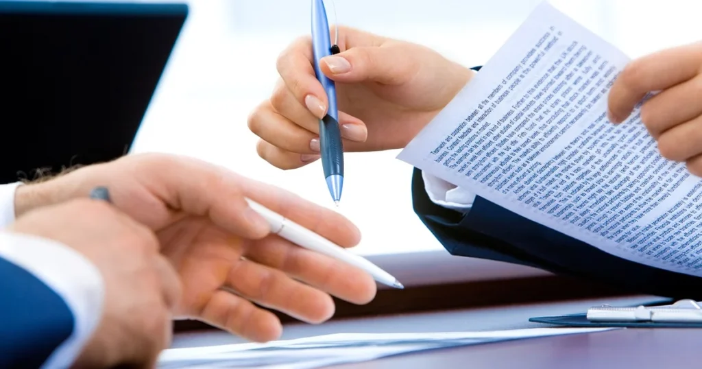 Deux personnes autour d'une table relisent un document papier, un stylo à la main, un ordinateur portable à côté